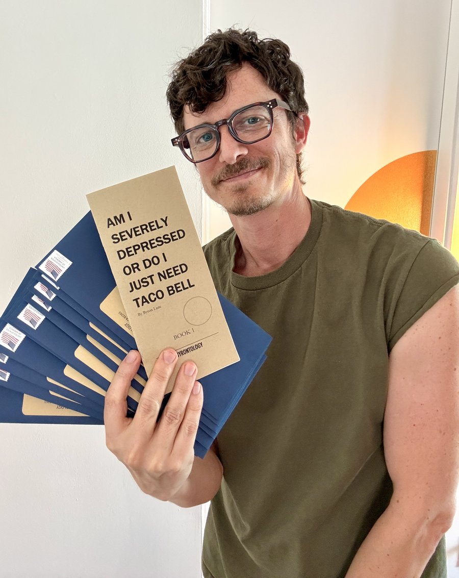 Byron Lane holding a handmade Byronbook and a fan of mailing envelopes