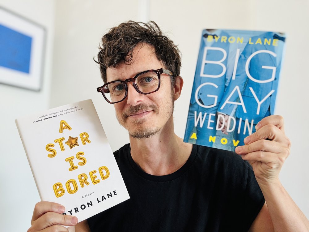 Byron Lane holding his novels A Star Is Bored and Big Gay Wedding